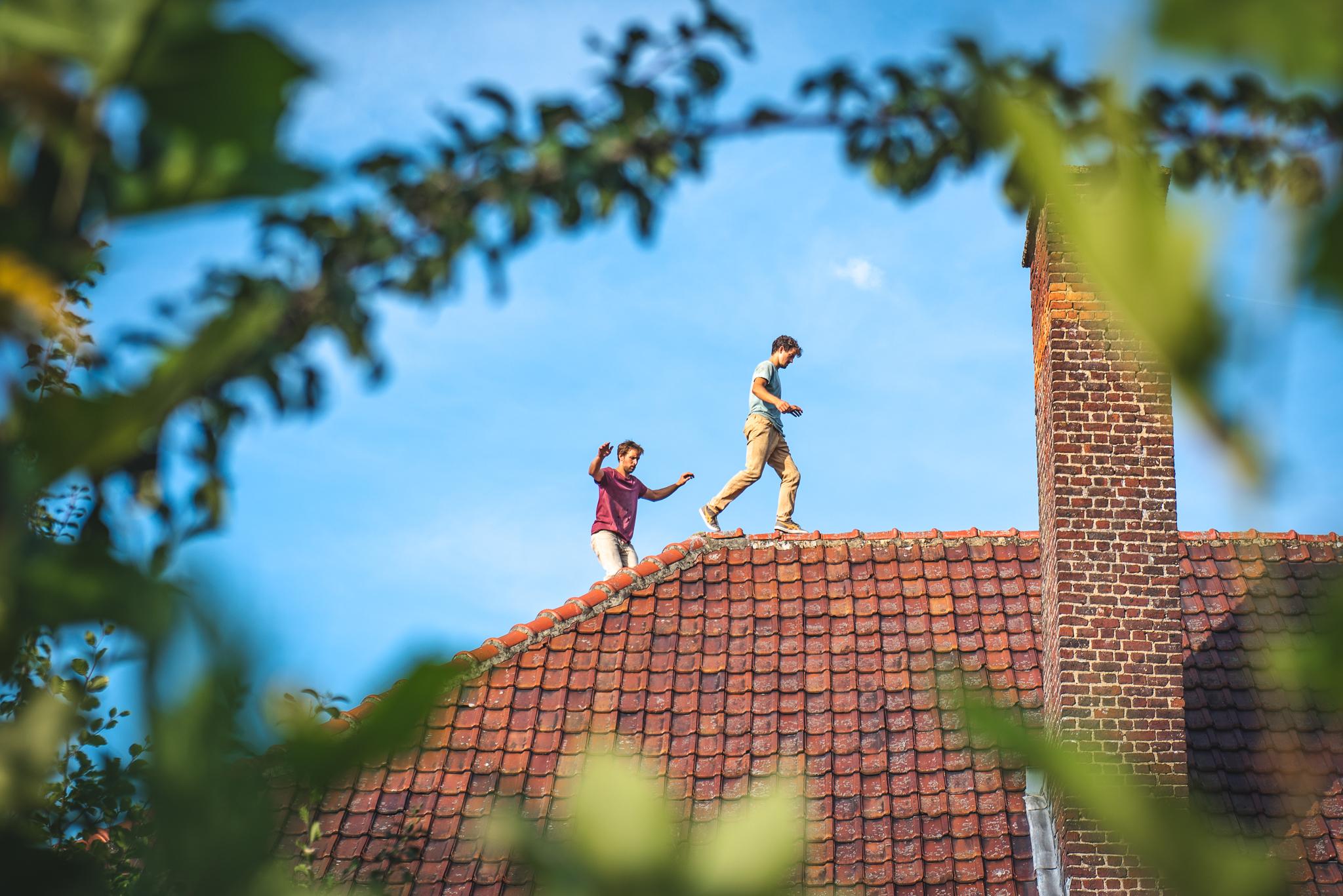 Two men walking on a rooftop made of red tiles.