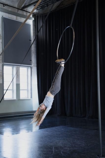 Circus artist hanging on the aerial hoop with her feet.